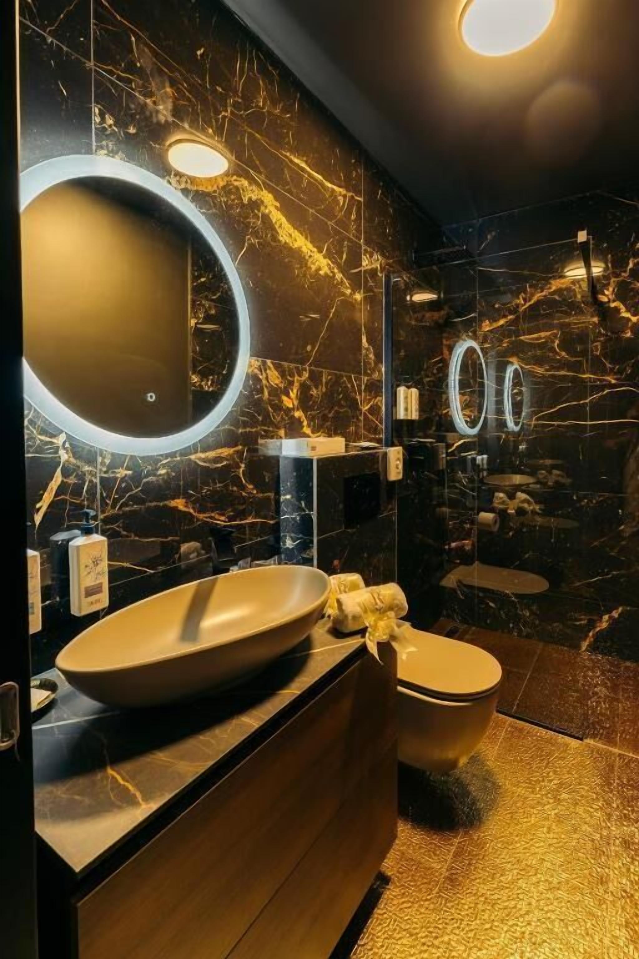 A modern bathroom with a large oval sink, two round mirrors, and a marble wall.