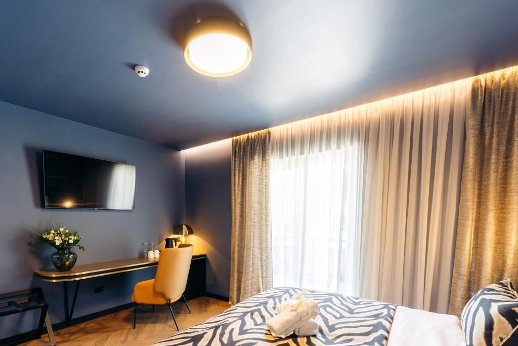 A hotel room with a bed, a desk, a chair, a TV, and a window with curtains.