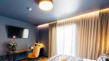A hotel room with a bed, a desk, a chair, a TV, and a window with curtains.