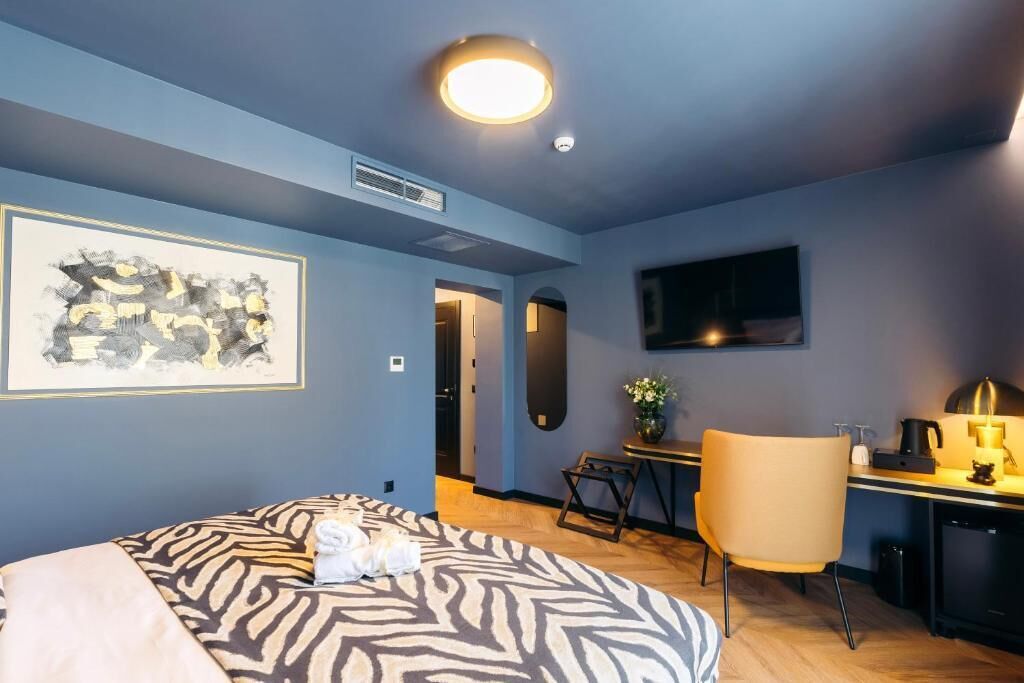 Habitación de hotel con cama, escritorio, silla, televisor y un cuadro en la pared.