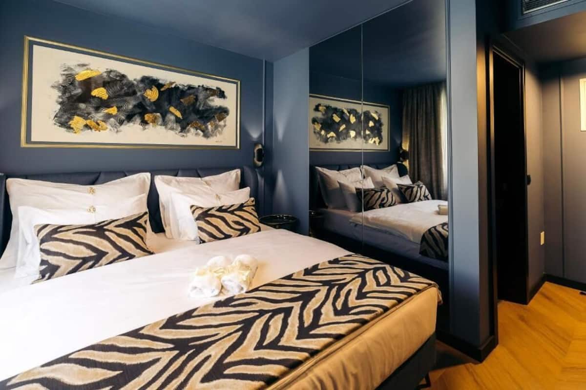 A hotel room with two beds, zebra-patterned bedding, abstract art on the walls, and a wooden floor.