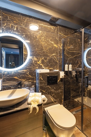 A modern bathroom with a marble wall, a round mirror, a toilet, and a glass shower enclosure.. Boutique Rooms Rogovo
