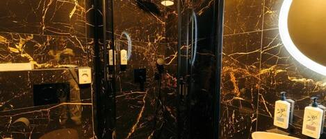 A bathroom with a black marble wall, a glass-enclosed shower, a sink, and toiletries.