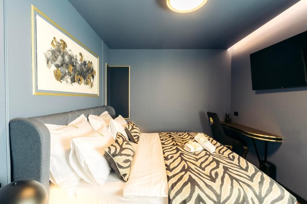 A modern hotel room with a bed, a desk, a chair, and a flat-screen TV on the wall.