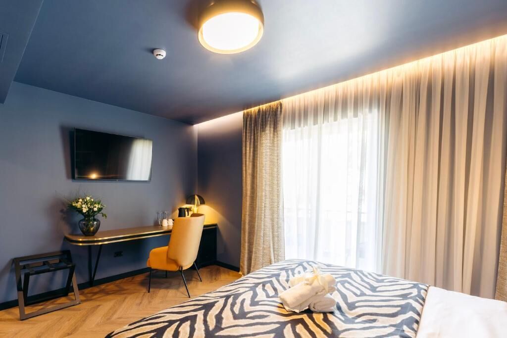 A hotel room with a bed, a desk, a chair, a TV, and a window with curtains.