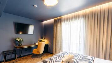 A hotel room with a bed, a desk, a chair, a TV, and a window with curtains.