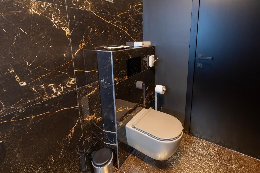 Un bagno moderno con una parete in marmo, un water, un cestino e una porta scura.