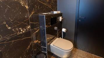 Un bagno moderno con una parete in marmo, un water, un cestino e una porta scura.