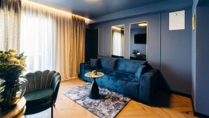 A modern living room with a dark blue sofa, a round coffee table, a green armchair, and a large window with curtains. - Boutique Rooms Rogovo (Sveti Filip i Jakov)