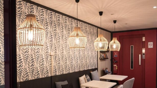 A restaurant interior with patterned wallpaper, multiple tables, and hanging light fixtures. - Hotel de Jouvence (Dax)