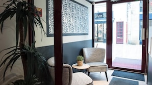 A reception area with a patterned wall, a potted plant, two wicker chairs, and a small table with a plant. - Hotel de Jouvence (Dax)