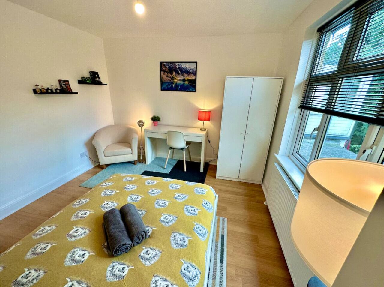 Ett kompakt hotellrum med en säng, ett skrivbord, en stol, ett element och ett fönster med persienner.