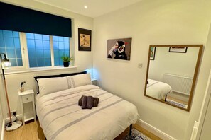 Ein Schlafzimmer mit Bett, Nachttisch, Lampe, Fenster und Spiegel.