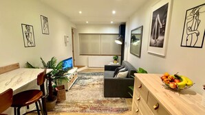 A modern living room with a dining area, a sofa, a coffee table with fruit, and artwork on the walls. - Chic one-bedroom London flat with parking & great links (Greater London)