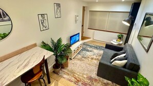 A modern living room with a TV, sofa, dining table, chairs, and a large window. - Chic one-bedroom London flat with parking & great links (Greater London)