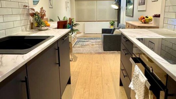 A modern kitchen with dark cabinets, white countertops, and a wooden floor. - Chic one-bedroom London flat with parking & great links (Greater London)