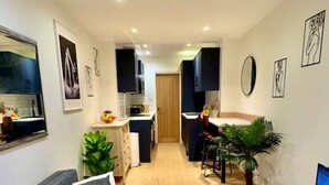 A modern living room with a grey sofa, a coffee table, and a TV on a wooden cabinet. There is a kitchen in the background with a dining area. - Chic one-bedroom London flat with parking & great links (Greater London)