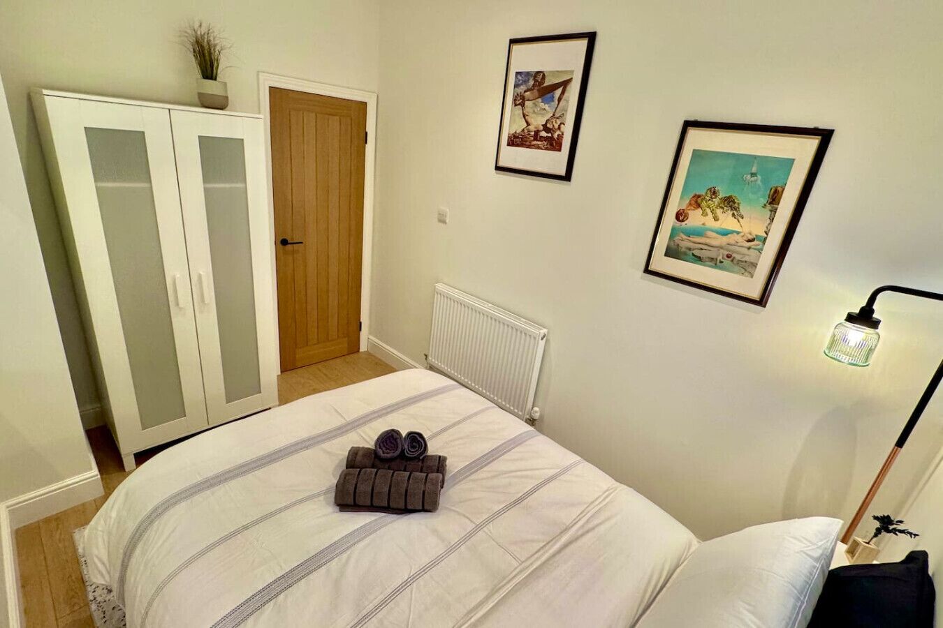 Un dormitorio con cama, armario, radiador y dos cuadros en la pared.