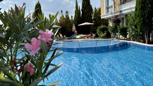 A swimming pool with lounge chairs and umbrellas, surrounded by tall trees and a building with balconies. - Menada Messembria Palace Apartments (Sunny Beach)