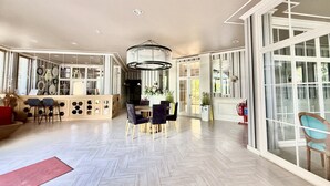 A spacious room with a herringbone floor, a central dining area with a chandelier, and large windows offering natural light. - Menada Messembria Palace Apartments (Sunny Beach)