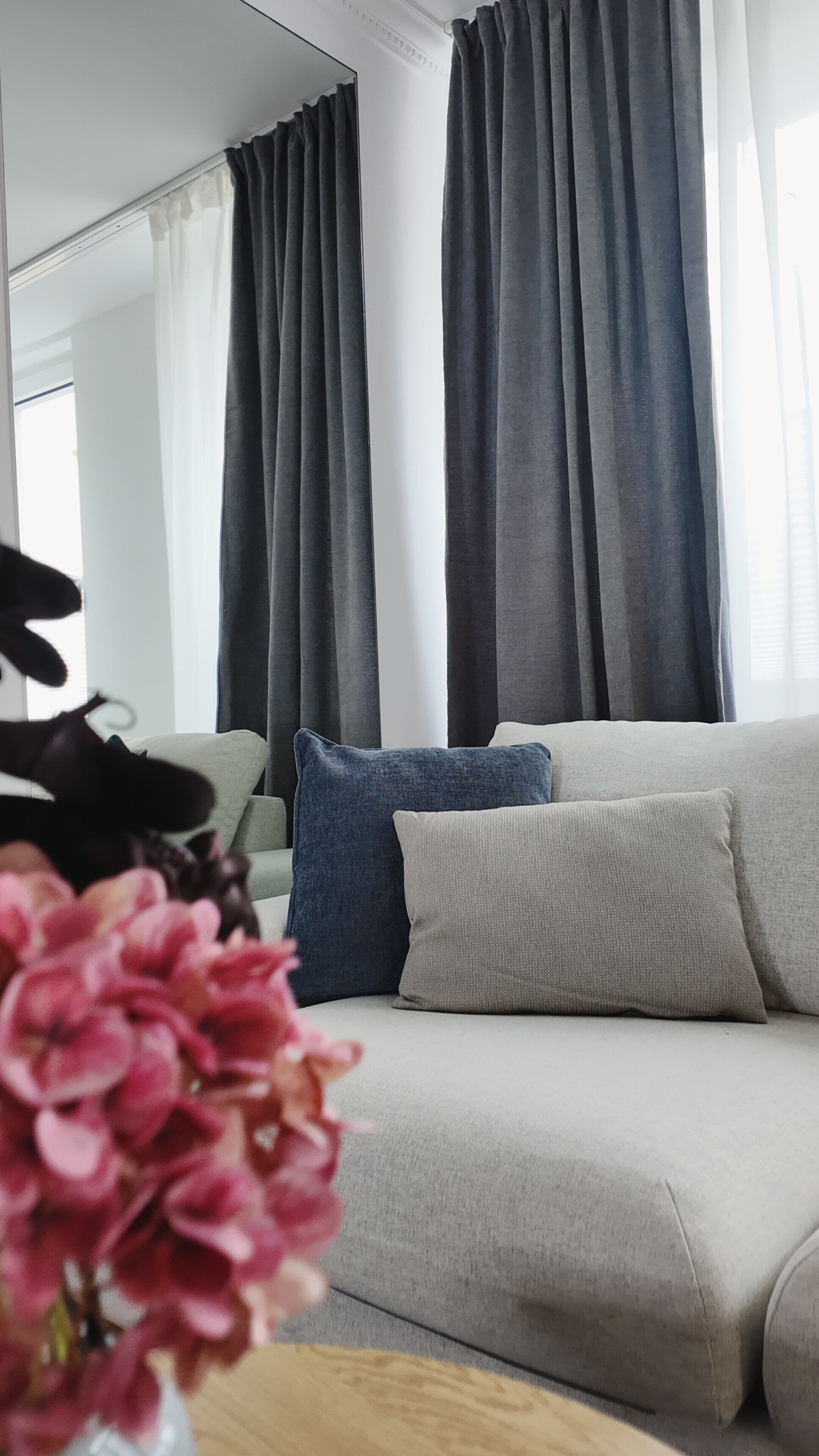 A modern living room with a sofa, a vase of flowers, and grey curtains.