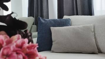 A modern living room with a sofa, a vase of flowers, and grey curtains.