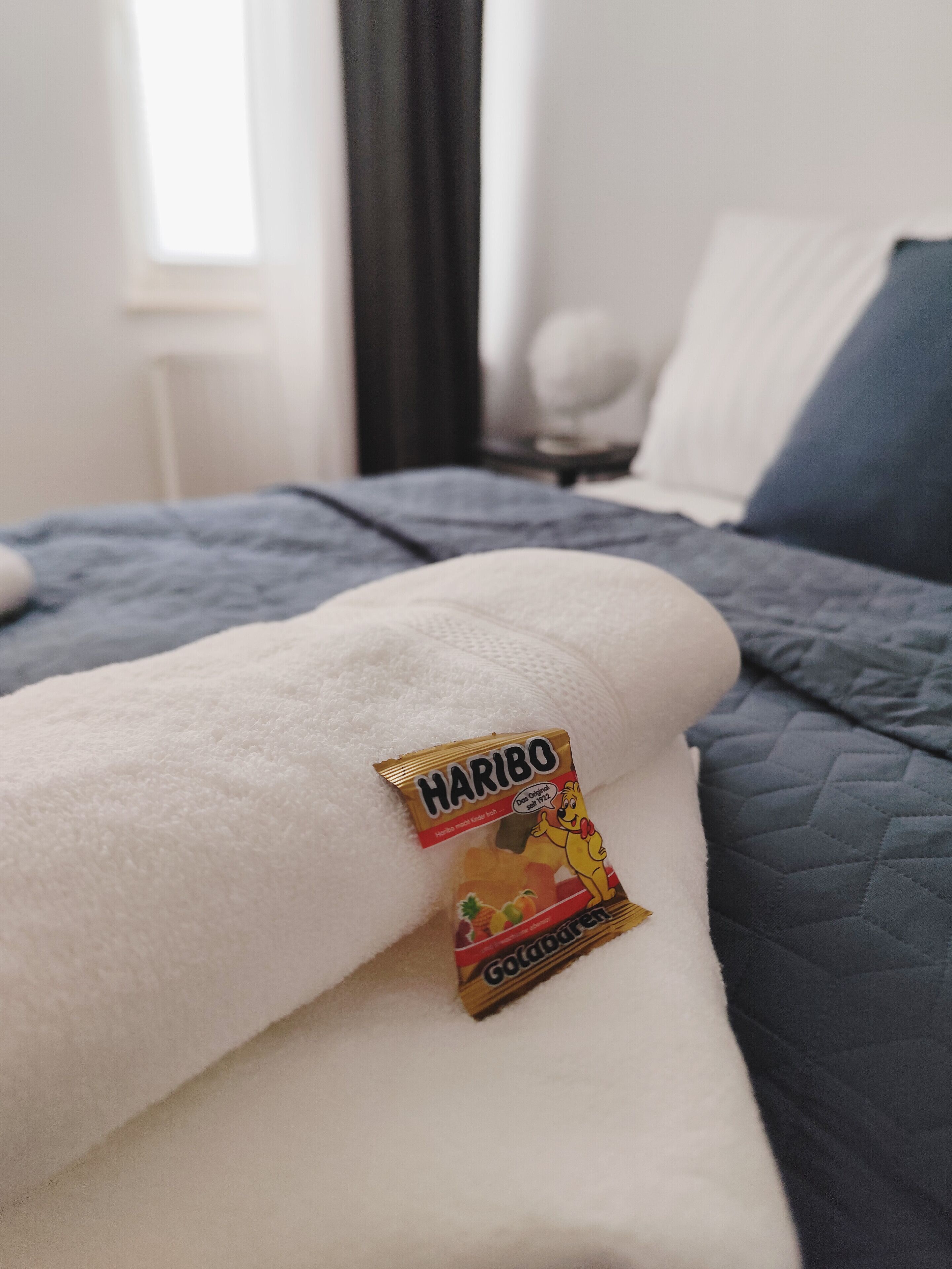 Un lit avec une couverture blanche et un paquet de bonbons Haribo GoGoGarten posé dessus.