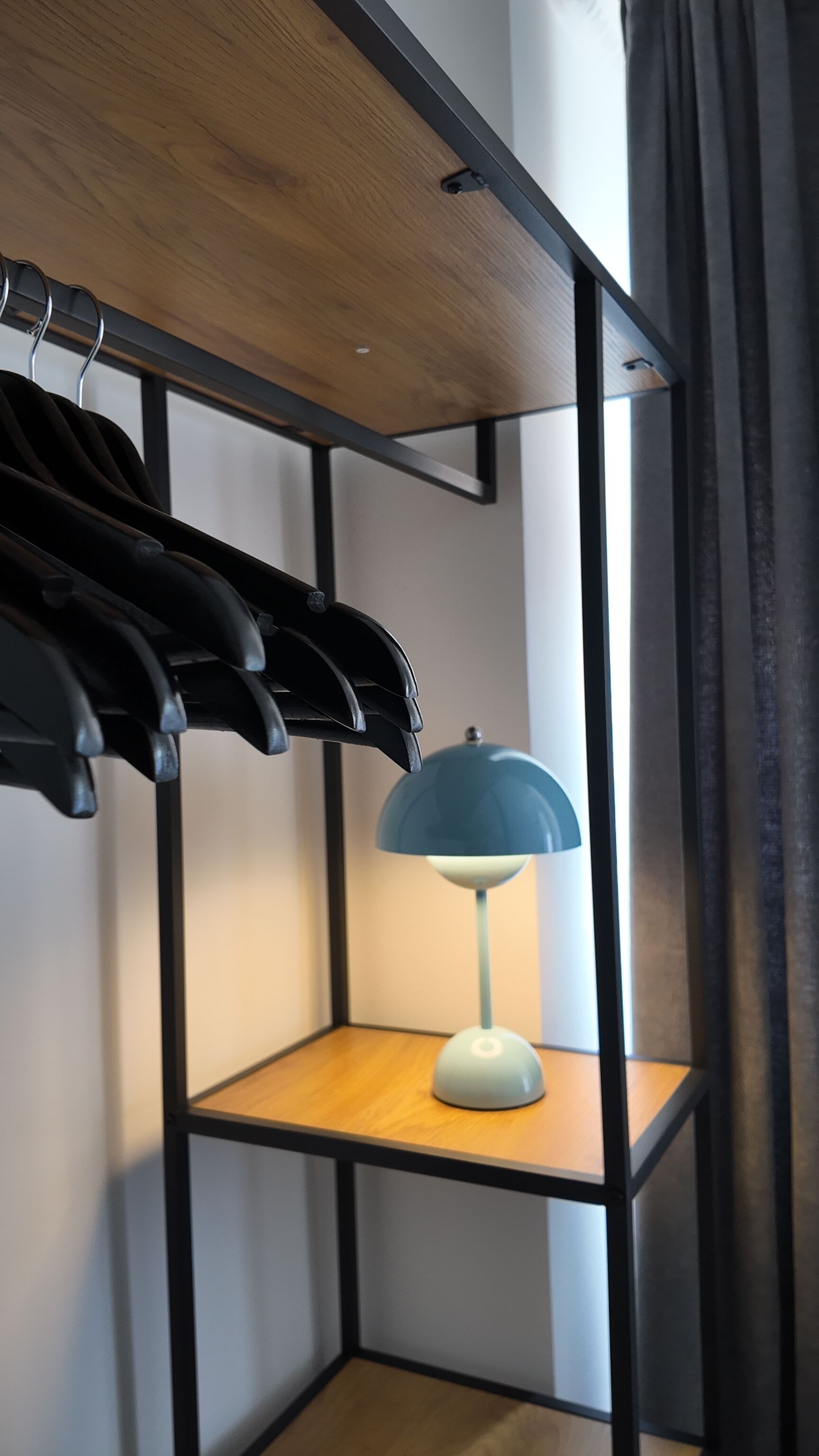 Ein Zimmer mit Holzboden, einem schwarzen Metallregal mit schwarzen Kleiderbügeln und einer blauen Lampe auf einem Holzboden.