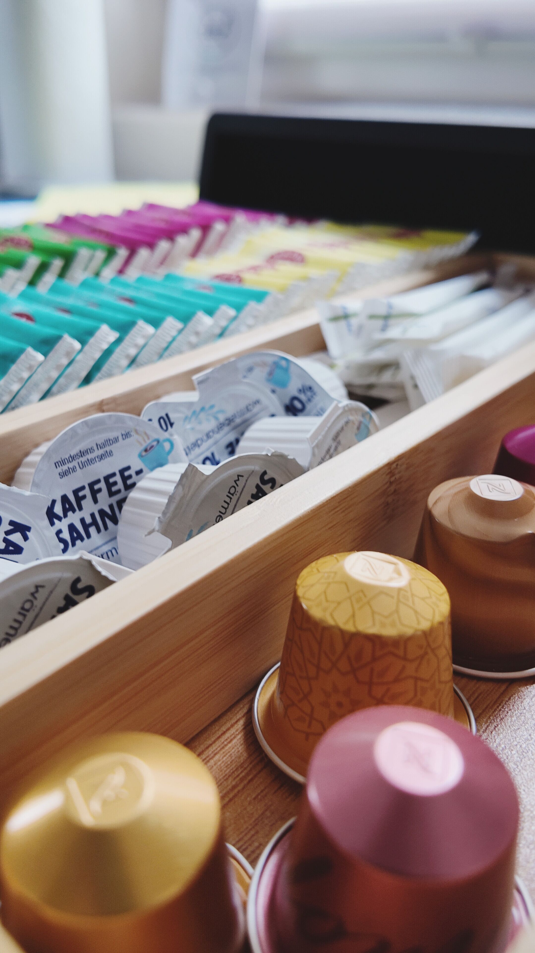 A wooden tray with various coffee pods and a few paper cups.