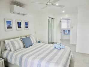 Ein Schlafzimmer mit Bett, Deckenventilator, Klimaanlage und gerahmten Bildern an der Wand.