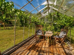 Een kas met een houten terras, twee stoelen en een tafel.