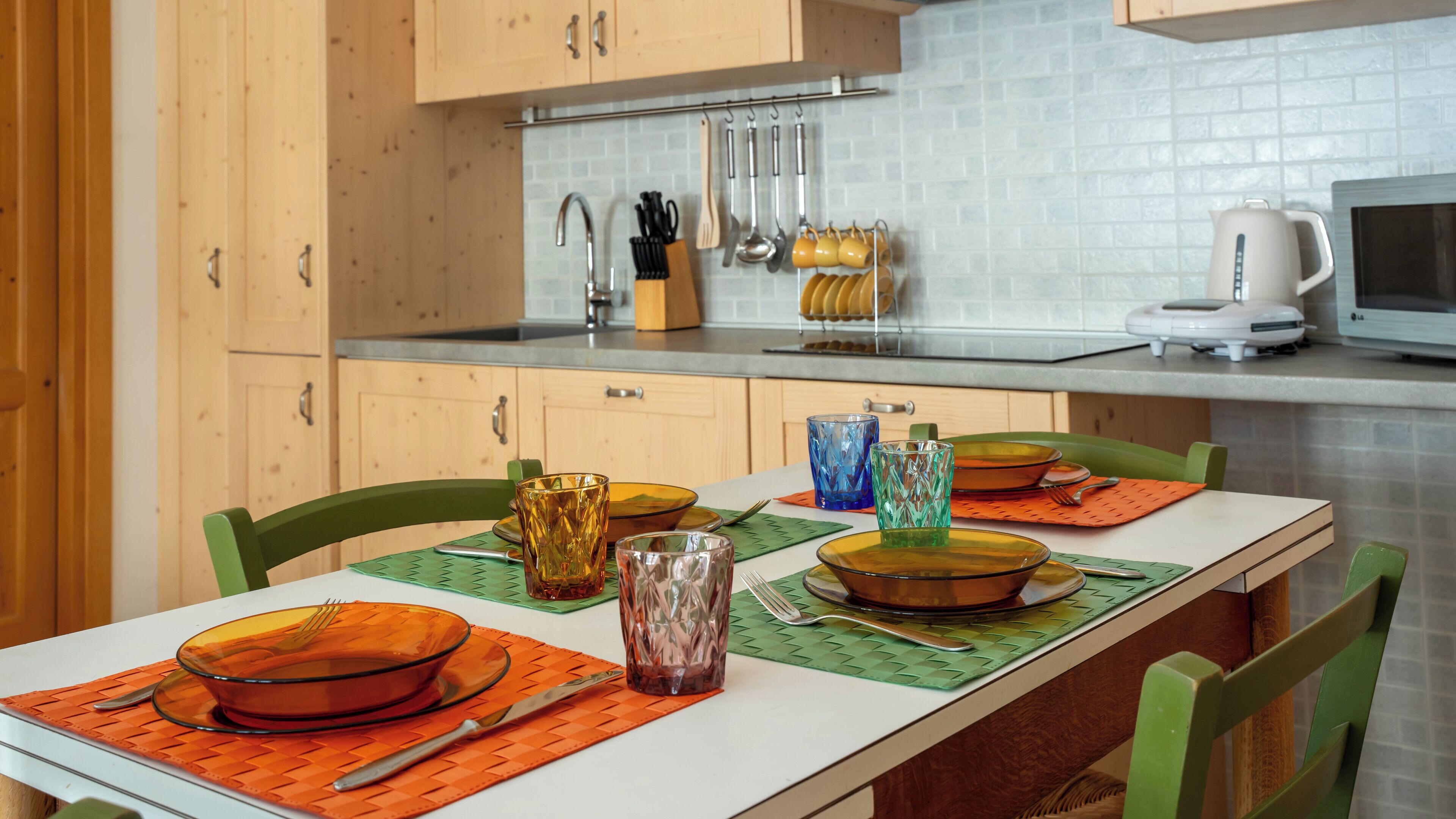 Une cuisine moderne avec des meubles en bois, un plan de travail blanc et un coin repas avec une table dressée pour quatre personnes.