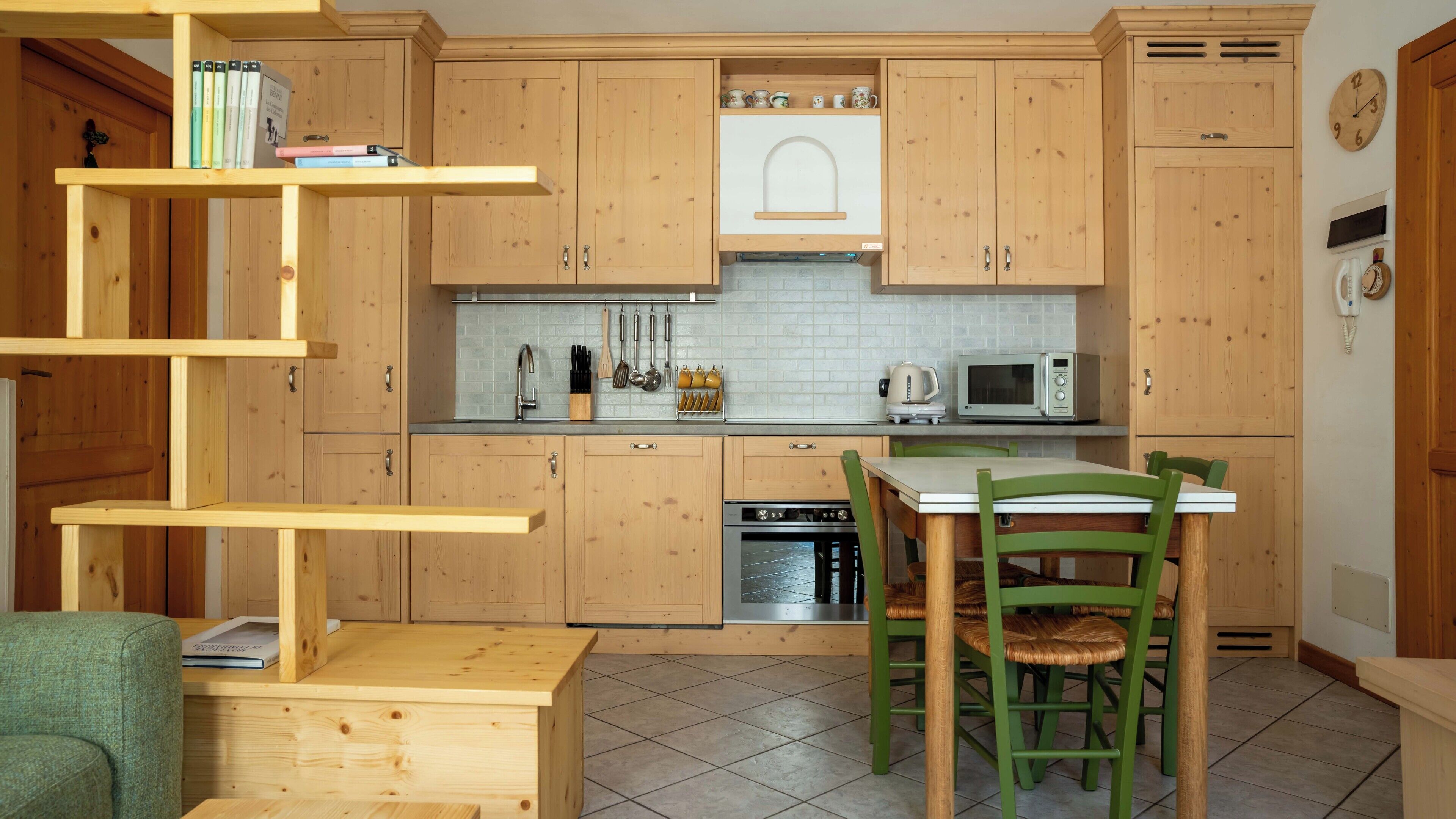 A kitchen with wooden cabinets, a microwave, a kettle, and a dining table with chairs.