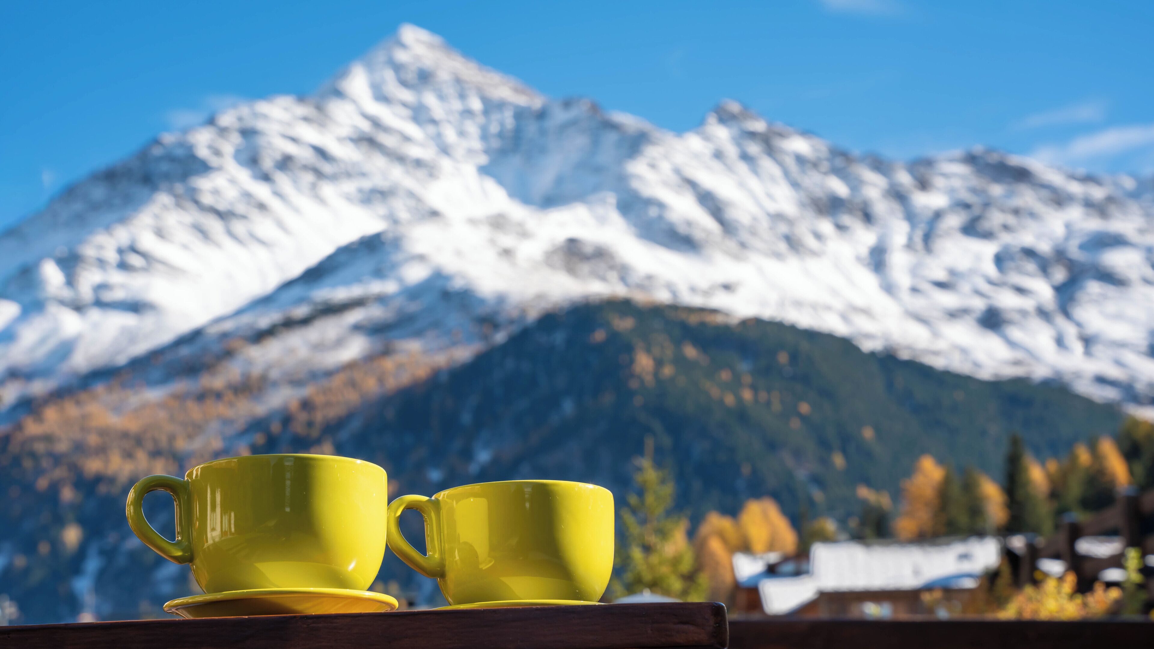 Two yellow cups on a wooden table with a mountain backdrop.