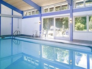 An indoor swimming pool with clear glass walls, a wooden ceiling, and a view of parked cars outside. - 4 Person Holiday Home in Nexo (Nexø)
