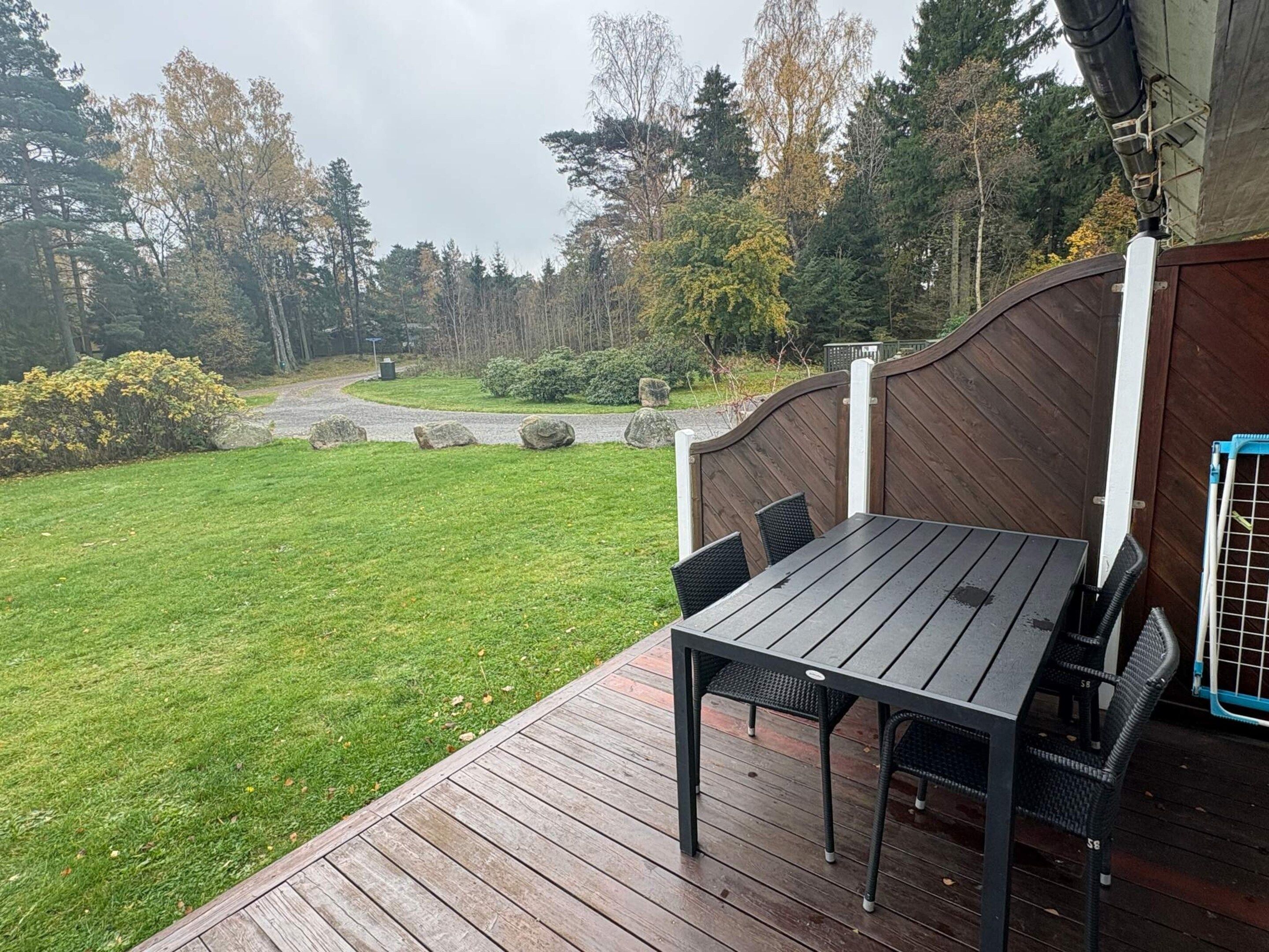 A wooden deck with a table and chairs, surrounded by a grassy lawn and trees.