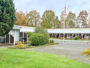 A motel with a covered outdoor seating area, a flagpole, and a grassy lawn. - 4 Person Holiday Home in Nexo (Nexø)