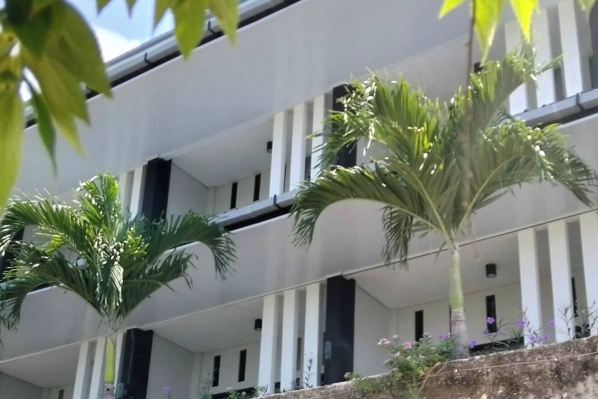 Un edificio de varios pisos con balcones, rodeado de follaje y plantas.