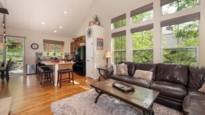 A spacious living area with a leather couch, wooden coffee table, and a view of the backyard through large windows.