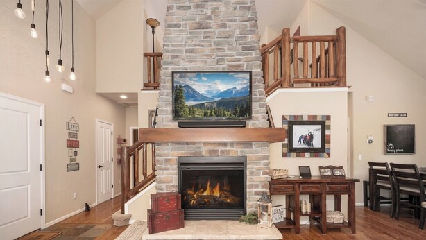 A living room with a stone fireplace, wooden staircase, and a flat-screen TV mounted above it.
