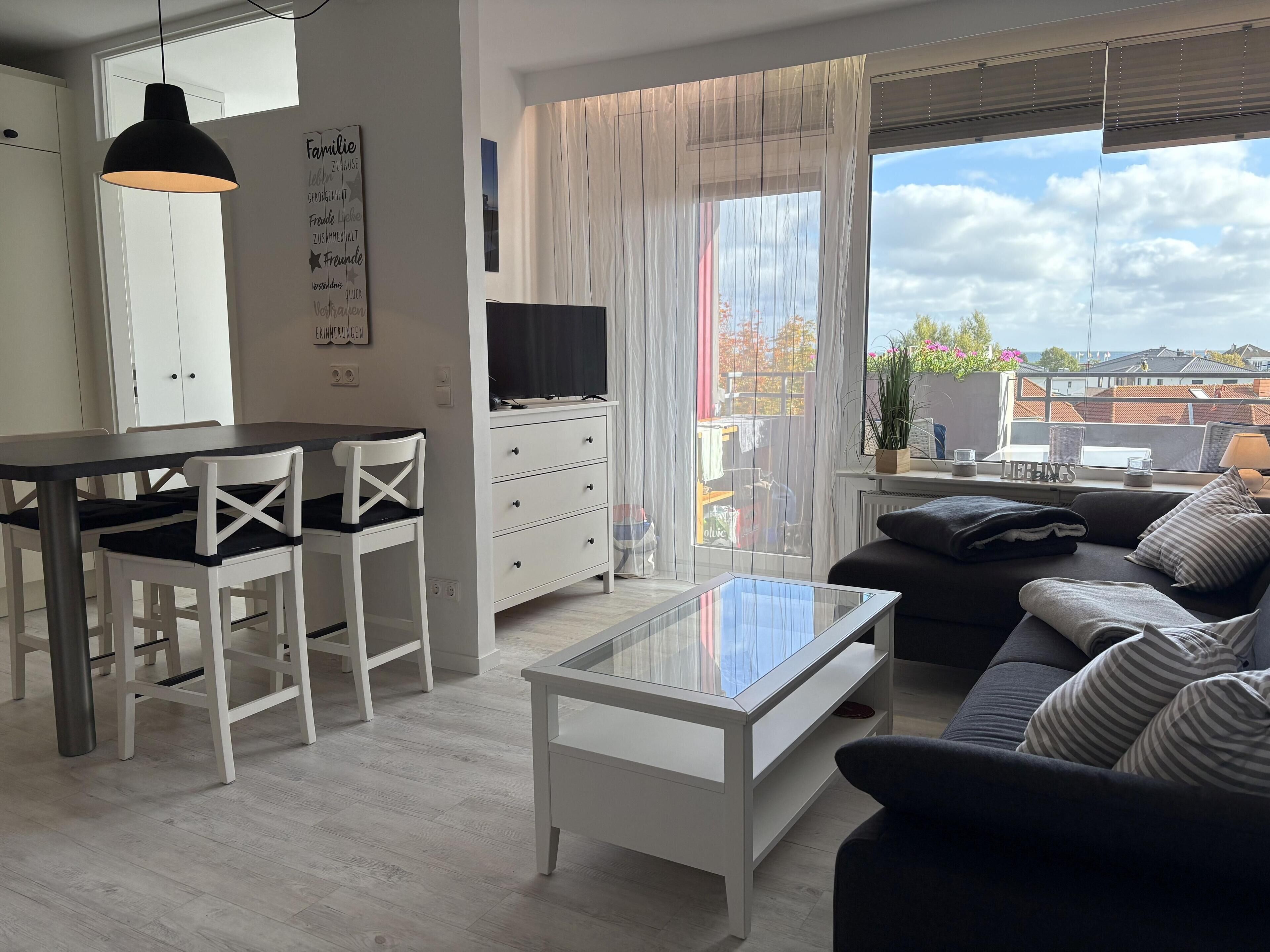A modern living room with a dining area, a sofa, a TV, and a large window with curtains.