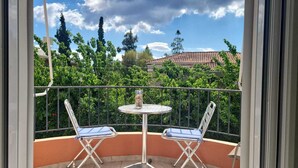 Un balcon avec deux chaises et une table, donnant sur un jardin et un bâtiment dont le toit est recouvert de tuiles.