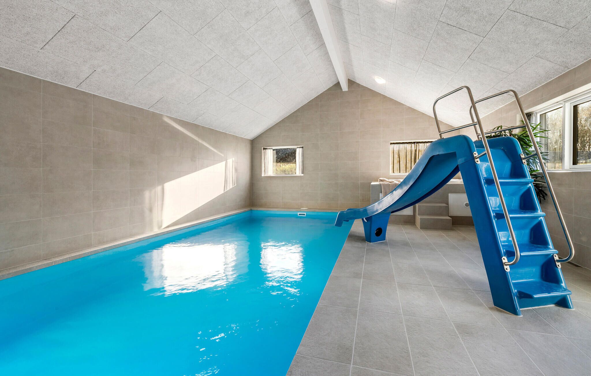 An indoor swimming pool with a blue slide and a ladder.
