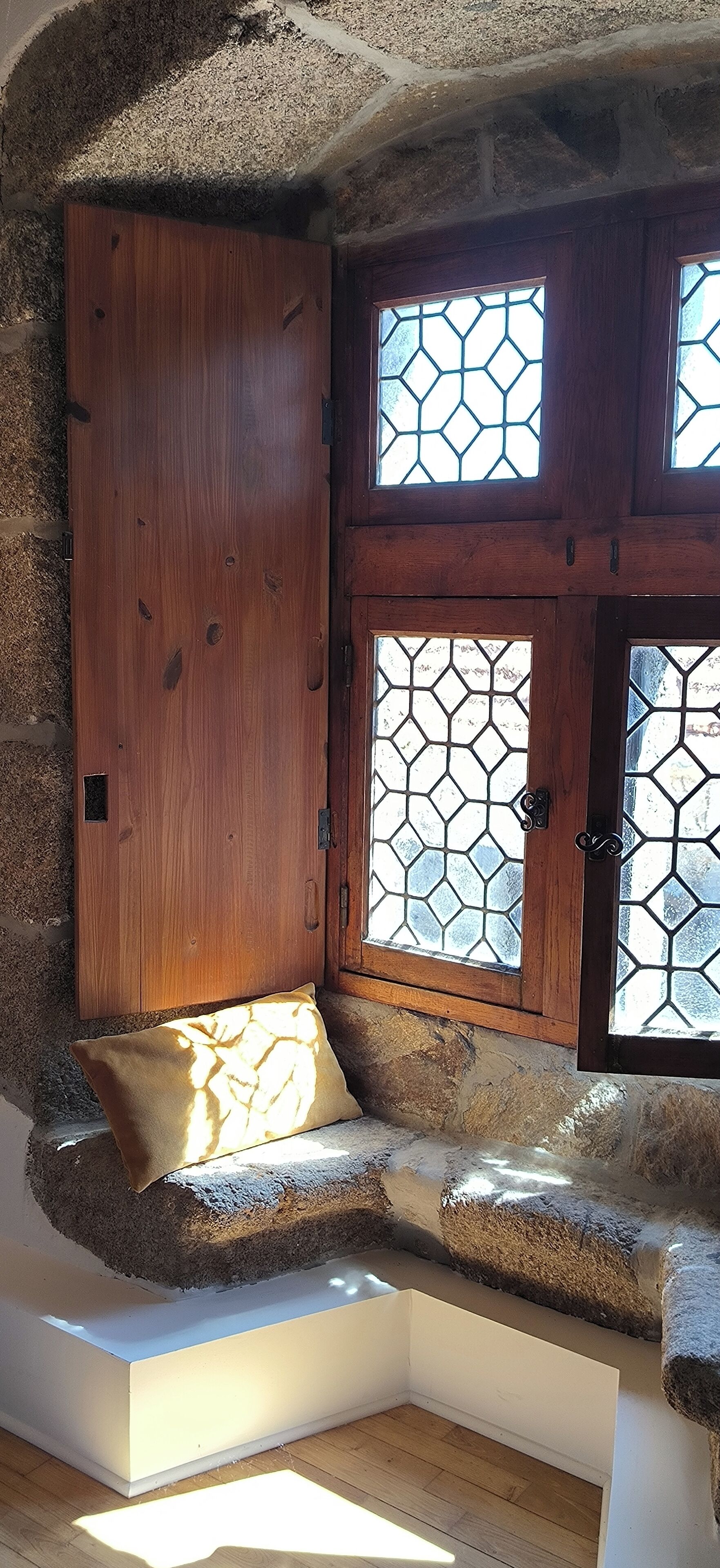 A stone bench with a cushion, a wooden door, and a window with a geometric pattern.