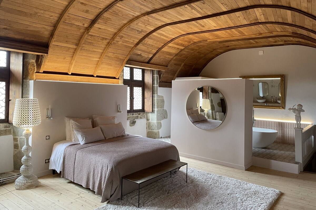 Ein Schlafzimmer mit Holzboden, einem Bett mit Kopfteil, einem runden Spiegel und einer Steinwand.