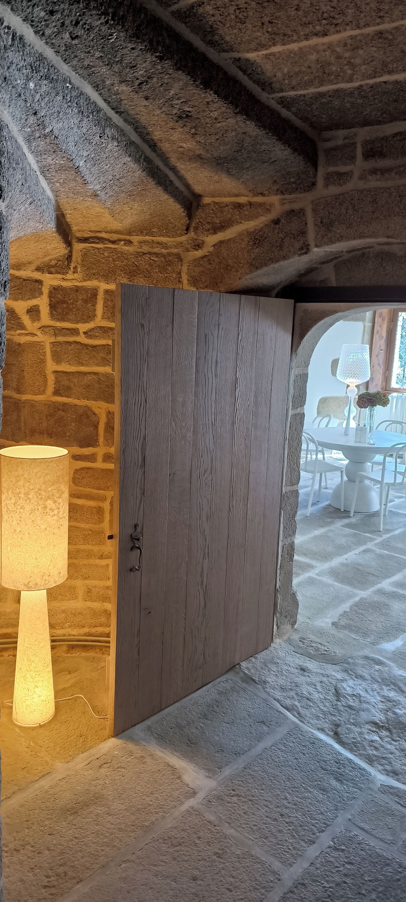 Un muro de piedra con una puerta de madera, una lámpara y un suelo de piedra.