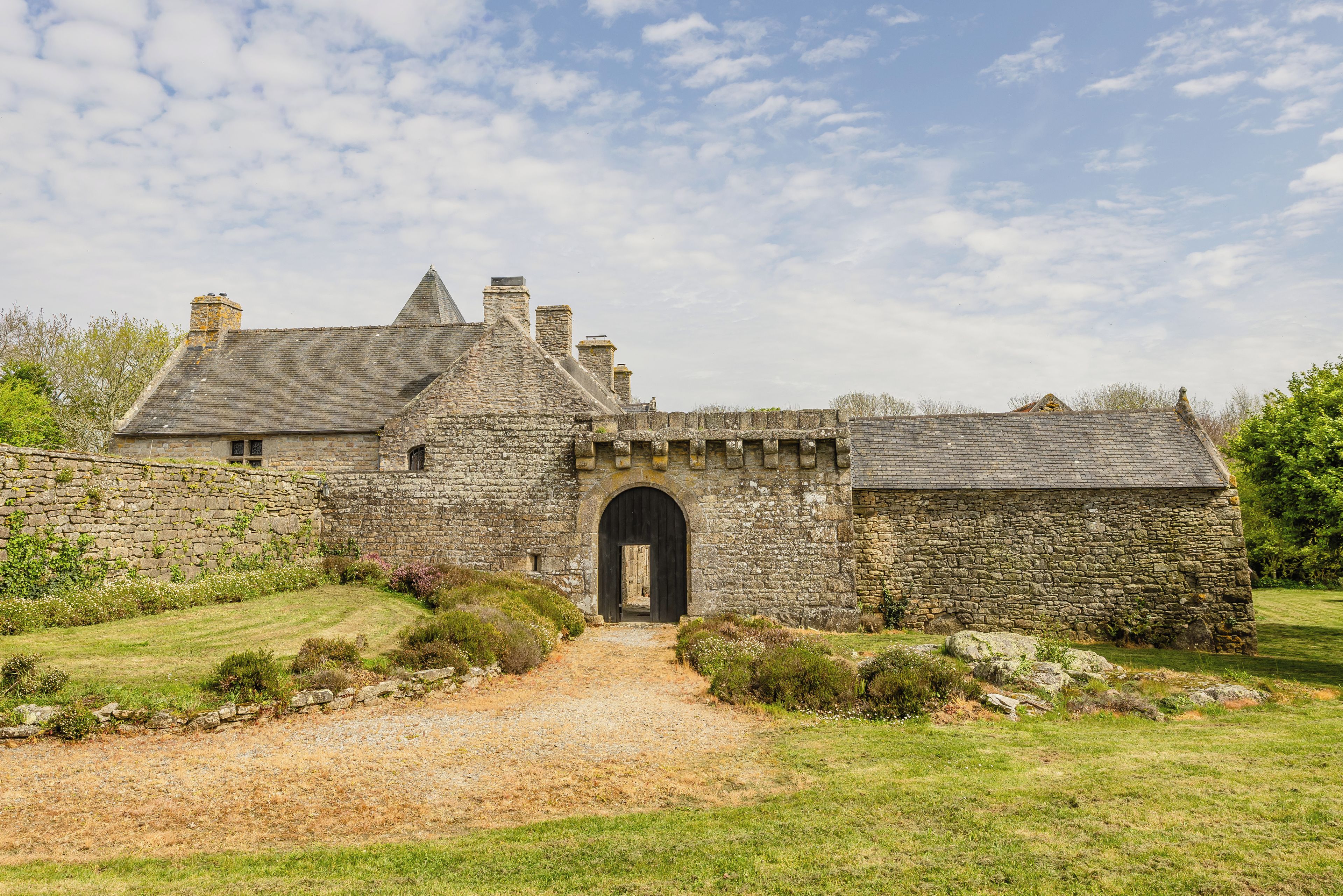 A stone building with a central archway, surrounded by a grassy area and a stone wall.