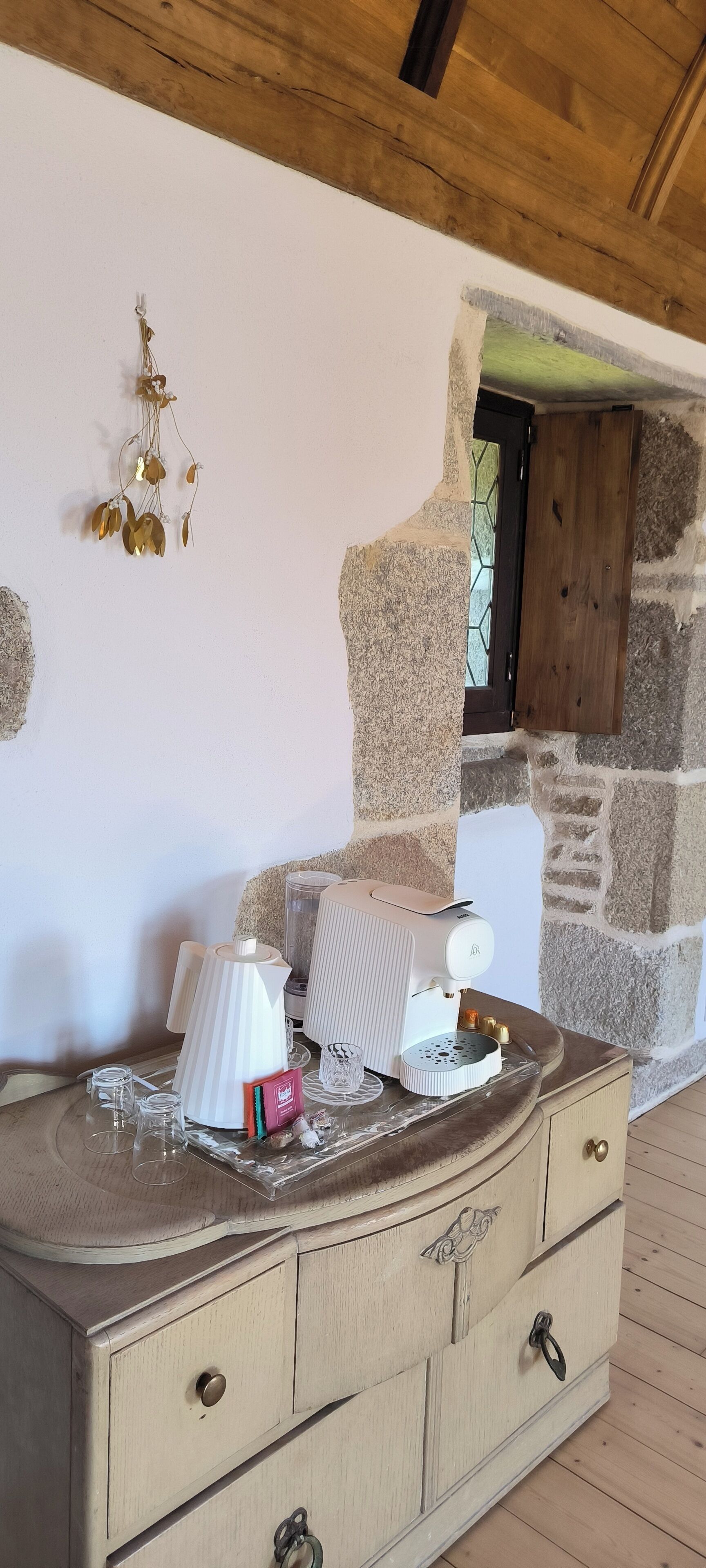 Een houten dressoir met een koffiezetapparaat, een waterkoker en een theeset. Achtergrond is een stenen muur en een houten deur.