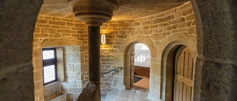 A stone interior with a central column, arched doorways, and a staircase.