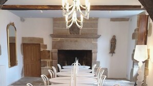A dining area with a round table surrounded by chairs, a chandelier, stone walls, and a fireplace. - Manoir de Kerenneur (Plourin)